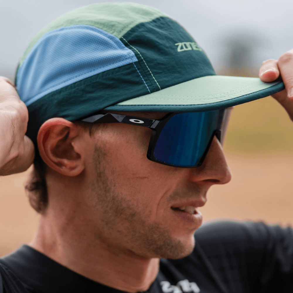 Man wearing a green and blue cap and sunglasses outdoors