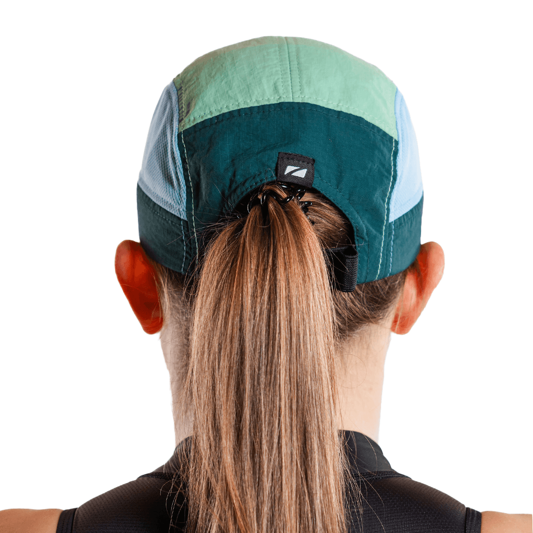 Gorra de running de 5 paneles en turquesa, llevada por una persona con coleta, sobre fondo blanco