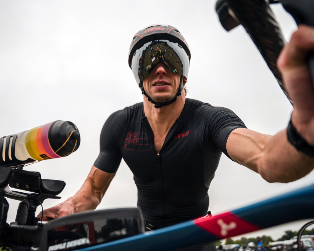 Person in triathlon gear with helmet and sunglasses and a bike.