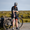 Hombre con el trisuit Activate+ de ZONE3 en negro, de pie junto a una bici de carretera, ajustándose la manga con casco y gafas de sol.