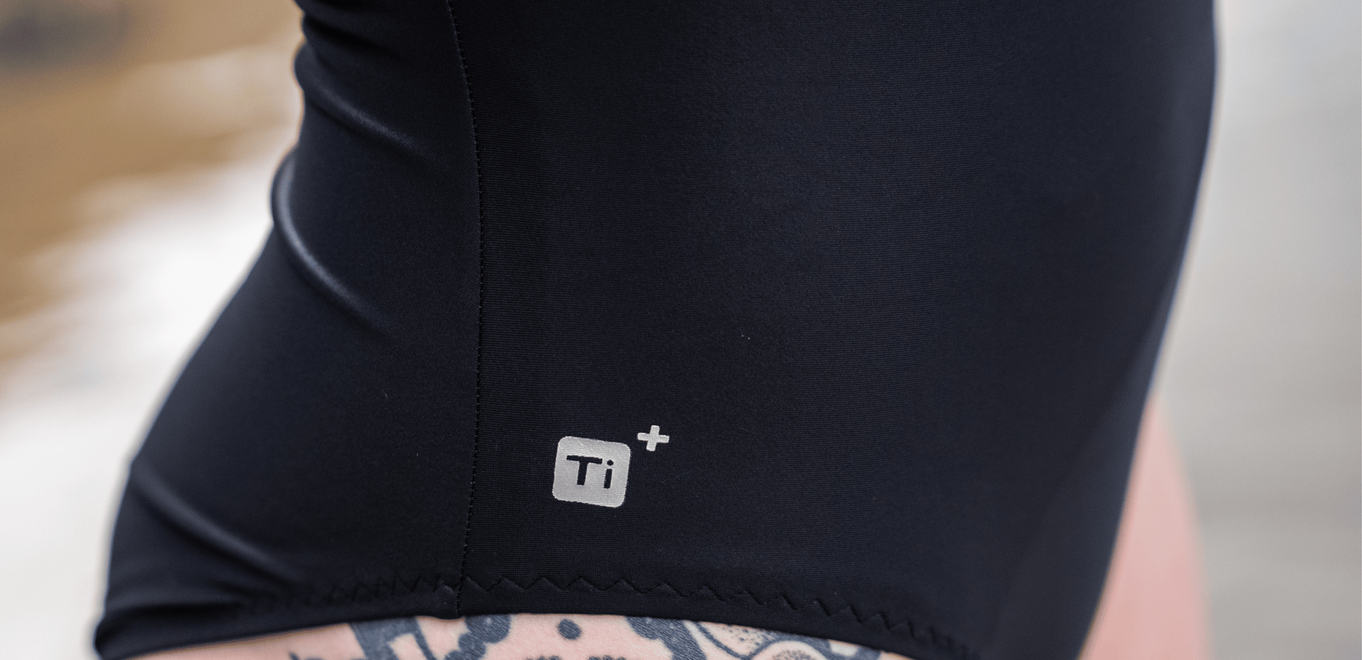 Close-up of a person wearing black TI+ thermal swimsuit with a logo on the leg.