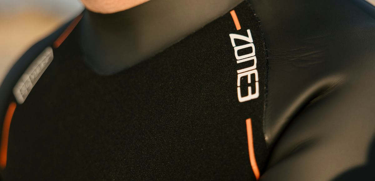 Close-up of a black sleeve of a wetsuit with 'Zone3' branding on an outdoor background