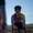 Mujer pedaleando de frente con el trisuit Activate+ de manga corta para mujer de ZONE3, gafas de sol espejadas y casco negro. El diseño degradado se aprecia claramente en el pecho y las mangas.