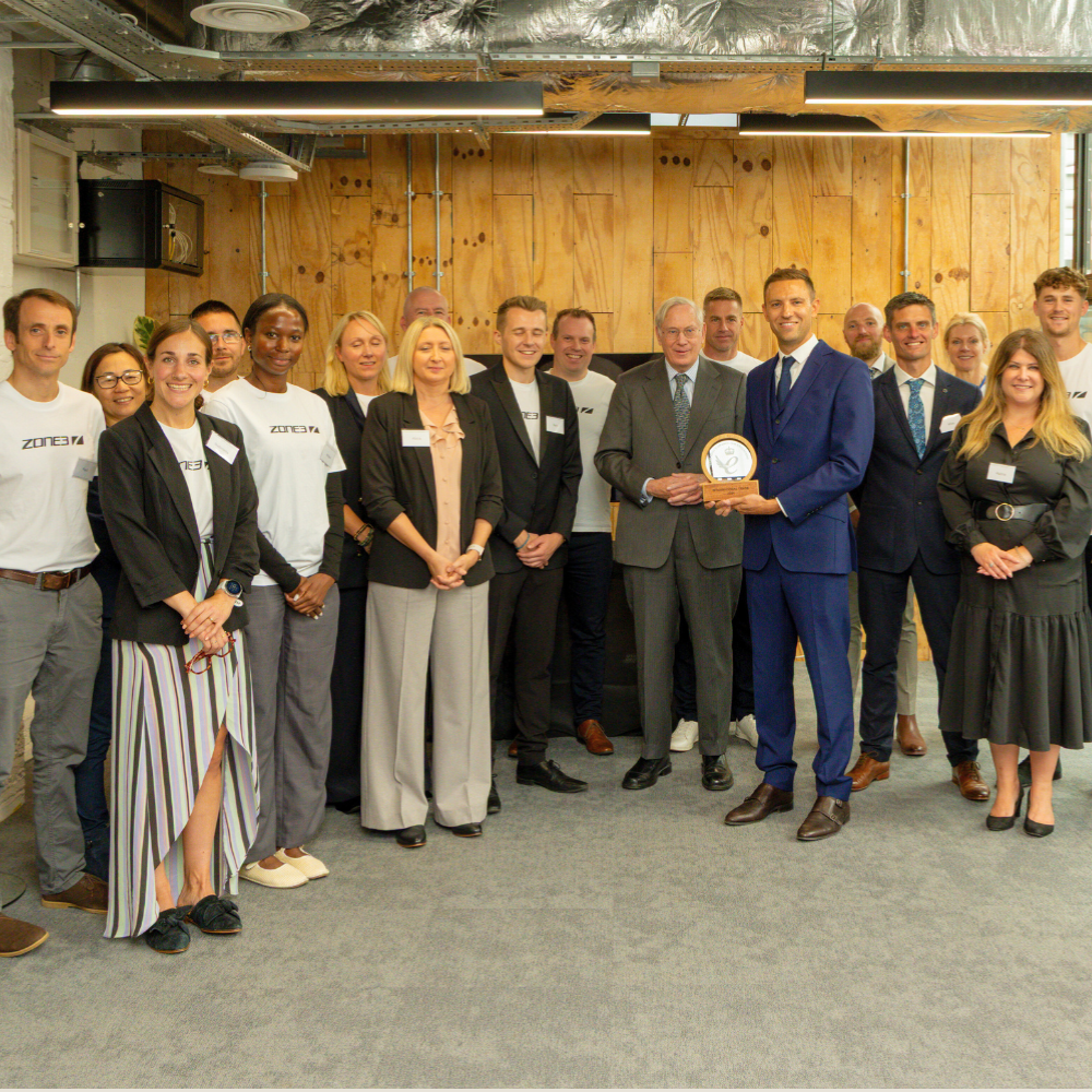 A picture of the ZONE3 team smiling for a photo. Centre of the image is founder James Lock with the Duke of Gloucestershire presenting the King's Award for Enterprise.