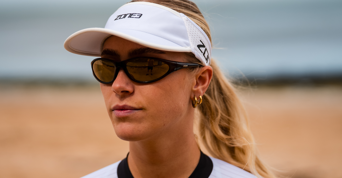 Woman wearing glasses and a zone3 white running visor with a zone3 logo on a blurred background