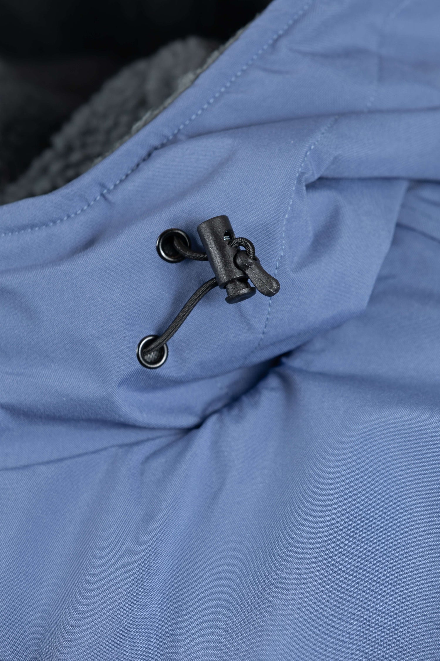 Detalle del cordón ajustable de la capucha y el cierre, sobre el tejido azul ártico.